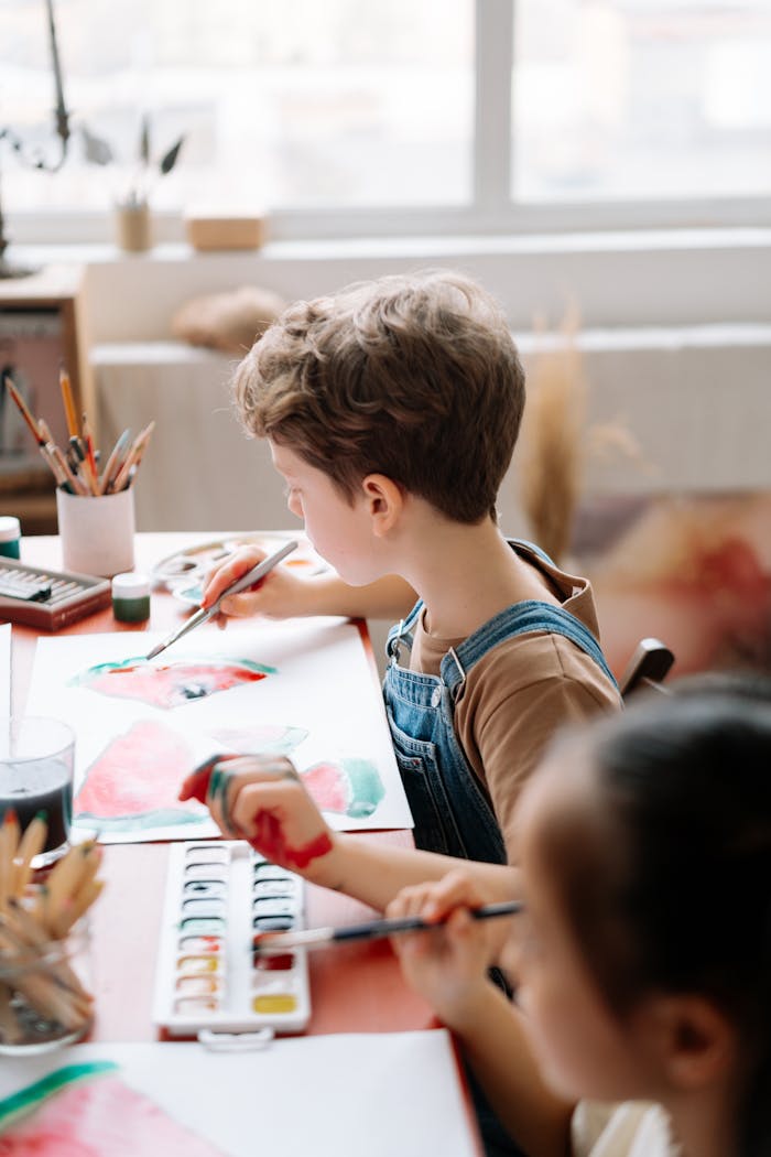 Children painting with watercolors in a sunny, indoor art workshop.