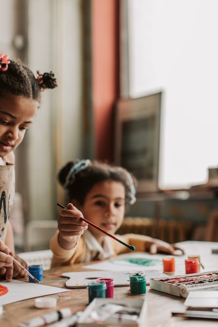 Two young girls engaged in a creative painting session indoors, using vibrant paints and brushes.