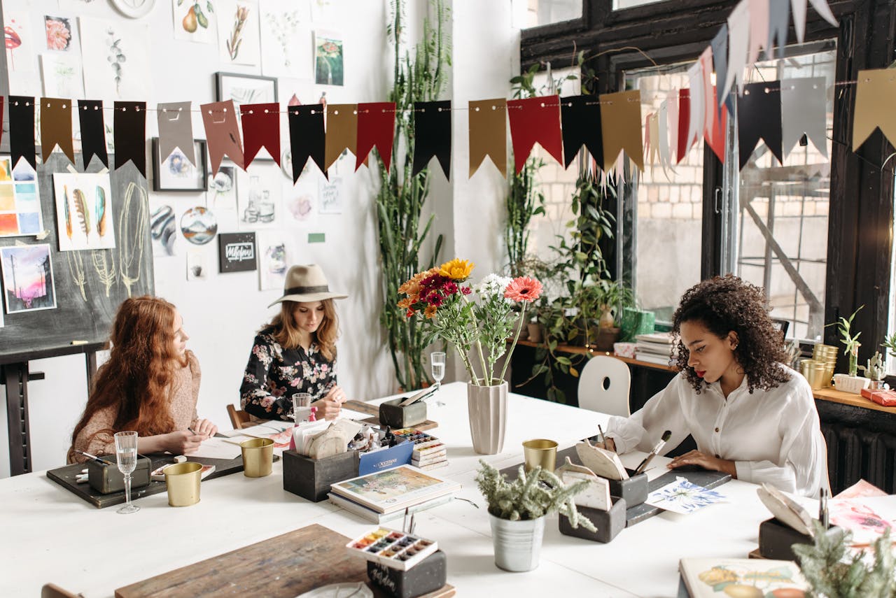 Three women engaged in a creative workshop, painting and drawing in a well-decorated studio space.